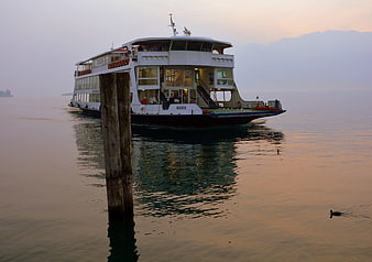 Ferry boat on calm lake at sunset with wooden post