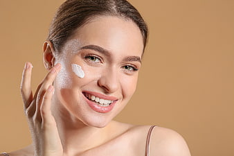 Smiling woman applying cream to cheek for skincare