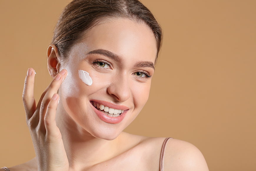 Smiling woman applying cream to cheek for skincare