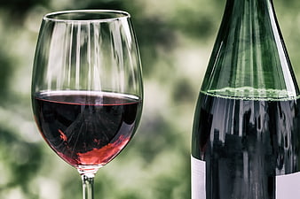 Red wine glass and bottle against blurred green background