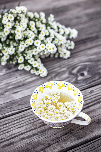 Chamomile tea in a floral cup with fresh flowers on a rustic wooden table