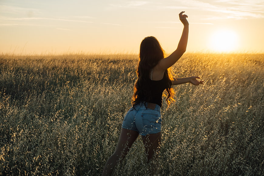 Woman dancing in wheat field at golden hour sunset