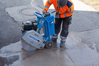 Construction worker operating blue concrete saw on asphalt road surface