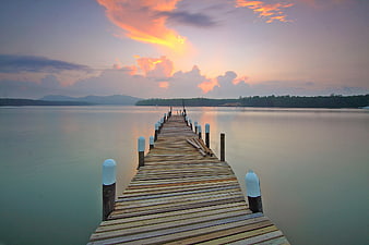 Wooden pier extending into calm sea at sunset with colorful clouds