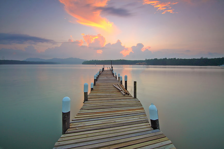 Wooden pier extending into calm sea at sunset with colorful clouds