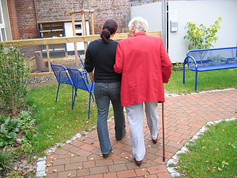Senior woman with walking stick and caregiver in care home garden