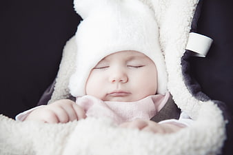 Sleeping newborn baby girl wearing a white fluffy hat and pink blanket