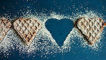 Heart-shaped waffles with powdered sugar on blue background