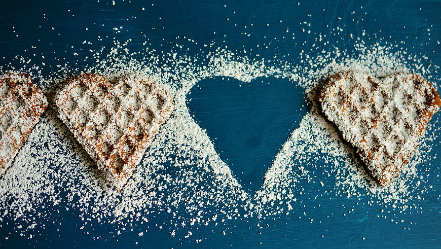 Heart-shaped waffles with powdered sugar on blue background