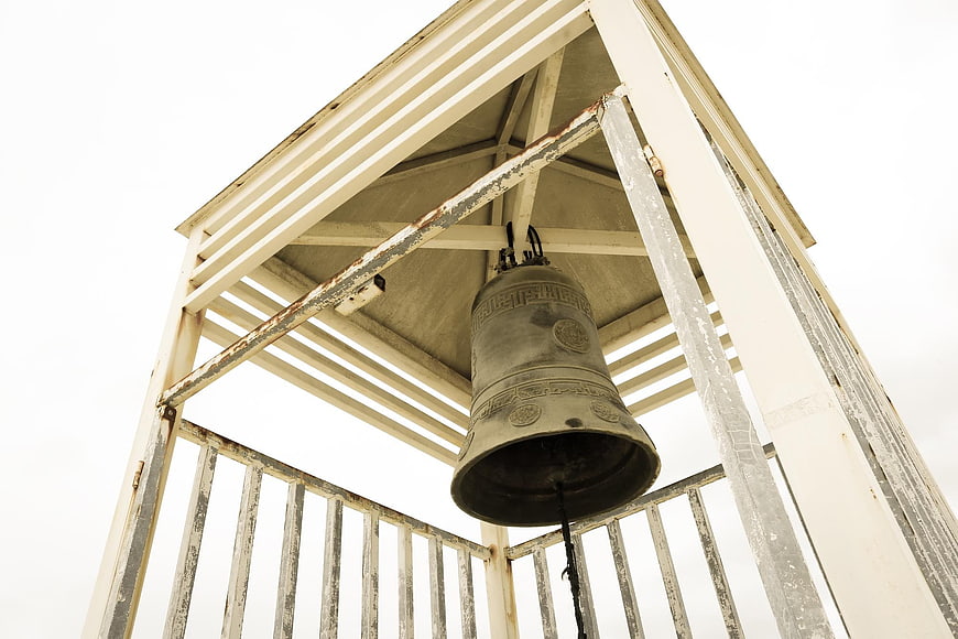 Low angle view of weathered bell in white wooden tower