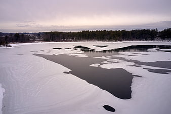 Aerial view of partially frozen lake with snow and forest