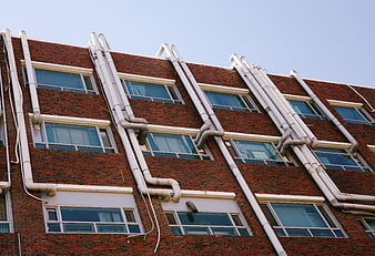 Low angle view of red brick building facade with white vertical pipes