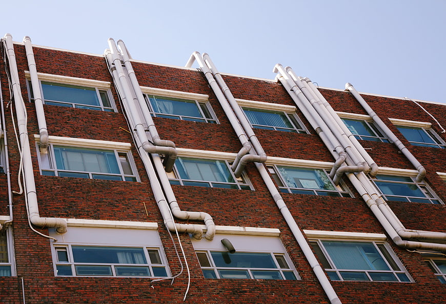 Low angle view of red brick building facade with white vertical pipes