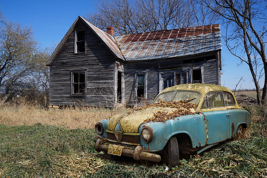 Abandoned Rusty Vintage Car in Front of Dilapidated House