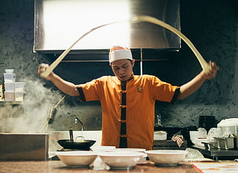 Asian chef tossing noodles in commercial kitchen