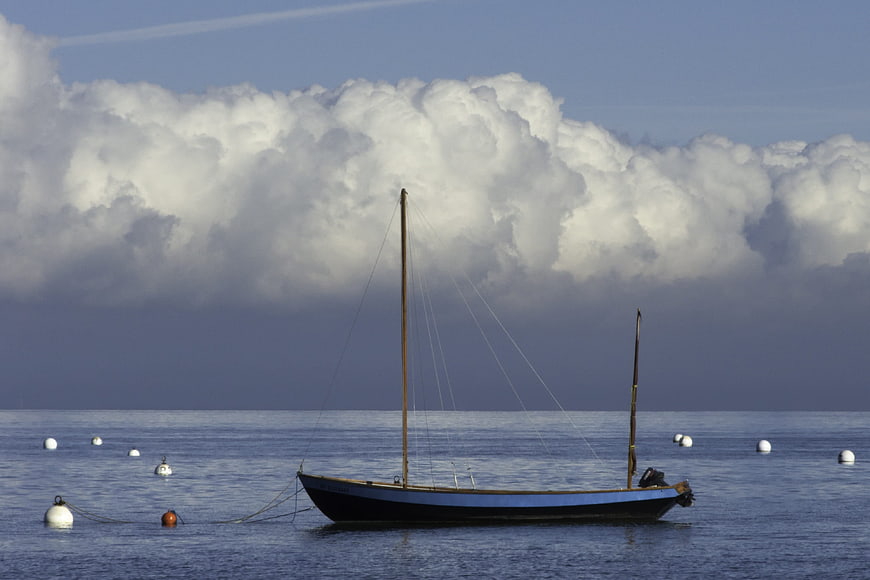Traditional sailing boat anchored in calm sea with dramatic clouds