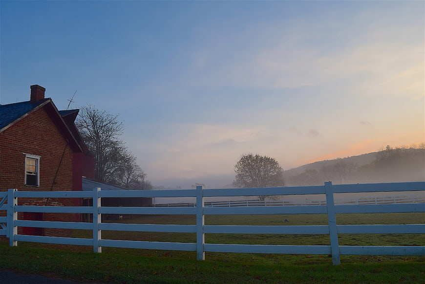 Misty Morning Farm Landscape with White Fence and Brick Barn