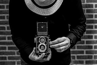 Man holding vintage Rolleicord TLR camera against brick wall