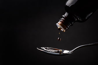 Dark amber liquid dripping from bottle into silver spoon