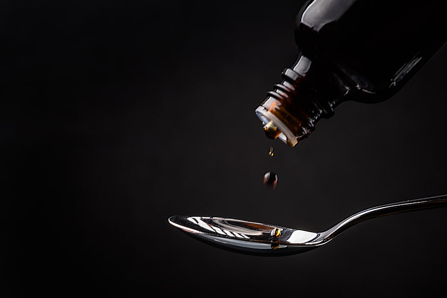 Dark amber liquid dripping from bottle into silver spoon