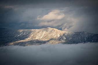 Snow-Capped Mountain Peak Emerging Through Thick Fog and Clouds
