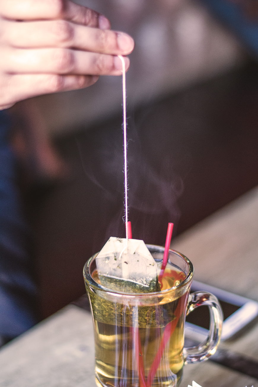 Hand dipping tea bag in steaming glass mug
