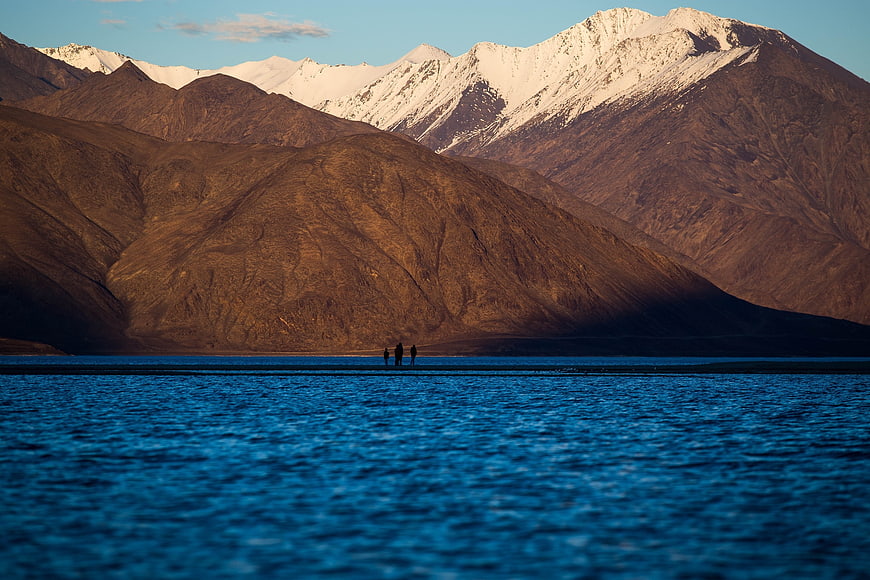 Silhouetted Hikers by Lake with Snow-Capped Mountains
