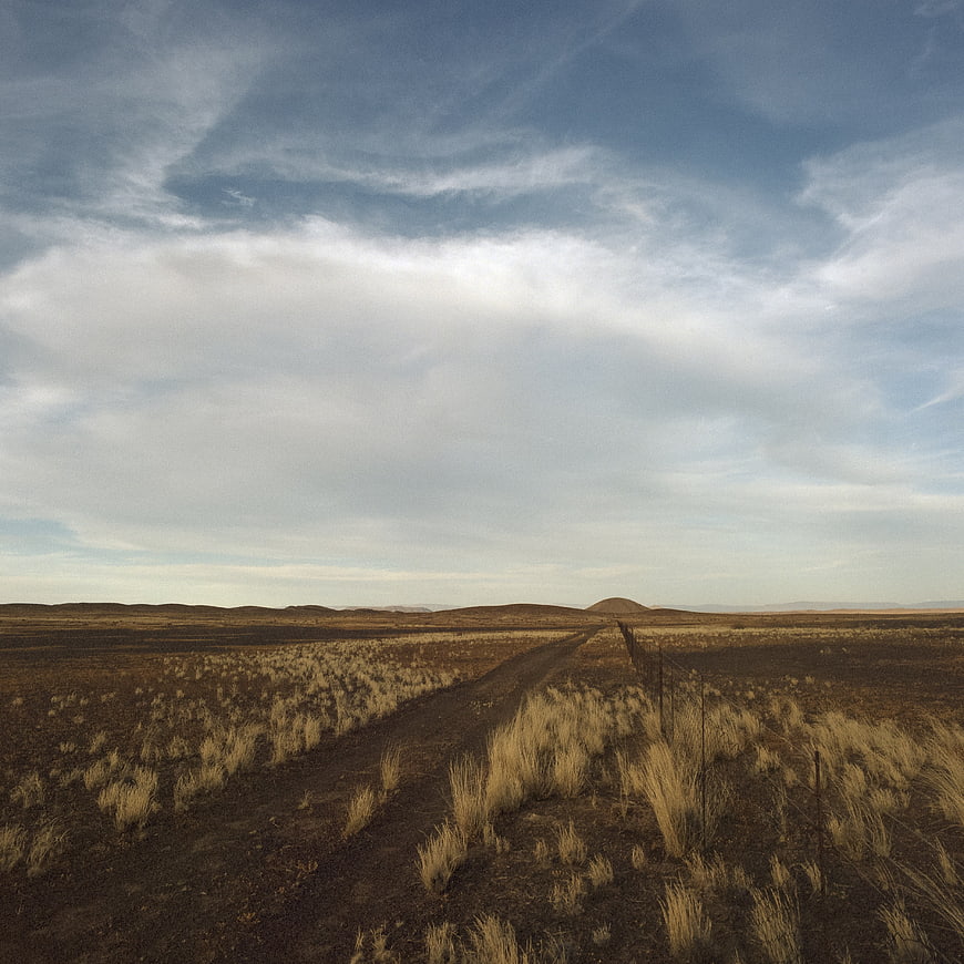 Dirt road stretching through arid landscape under cloudy sky