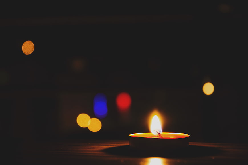 Single lit tea light candle with colorful bokeh background