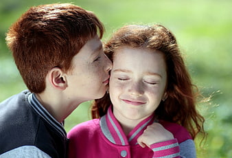 Red-haired boy kissing girl on cheek outdoors