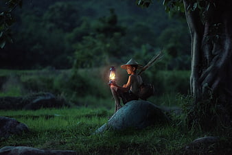 Young boy with lantern sitting on rock in forest at dusk