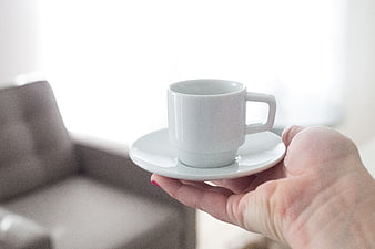 Hand holding white coffee cup on saucer with bright background