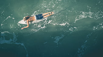 Aerial view of surfer paddling on surfboard in ocean