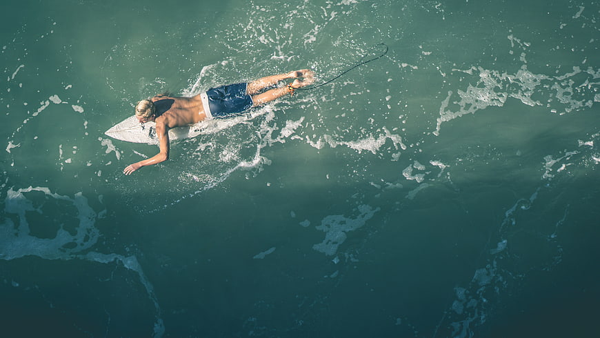 Aerial view of surfer paddling on surfboard in ocean