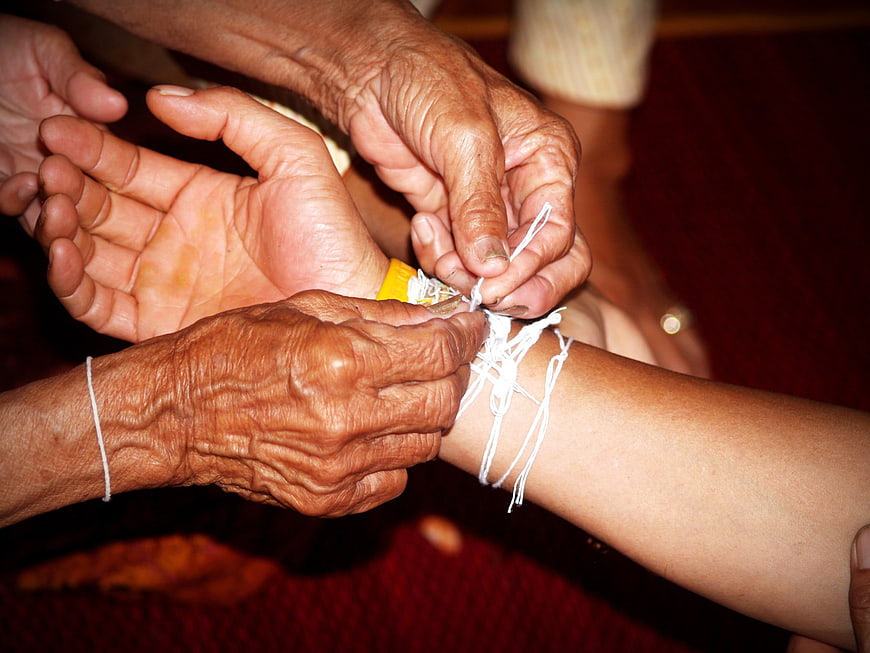 Elderly hands tying white thread around young person's wrist in a close-up
