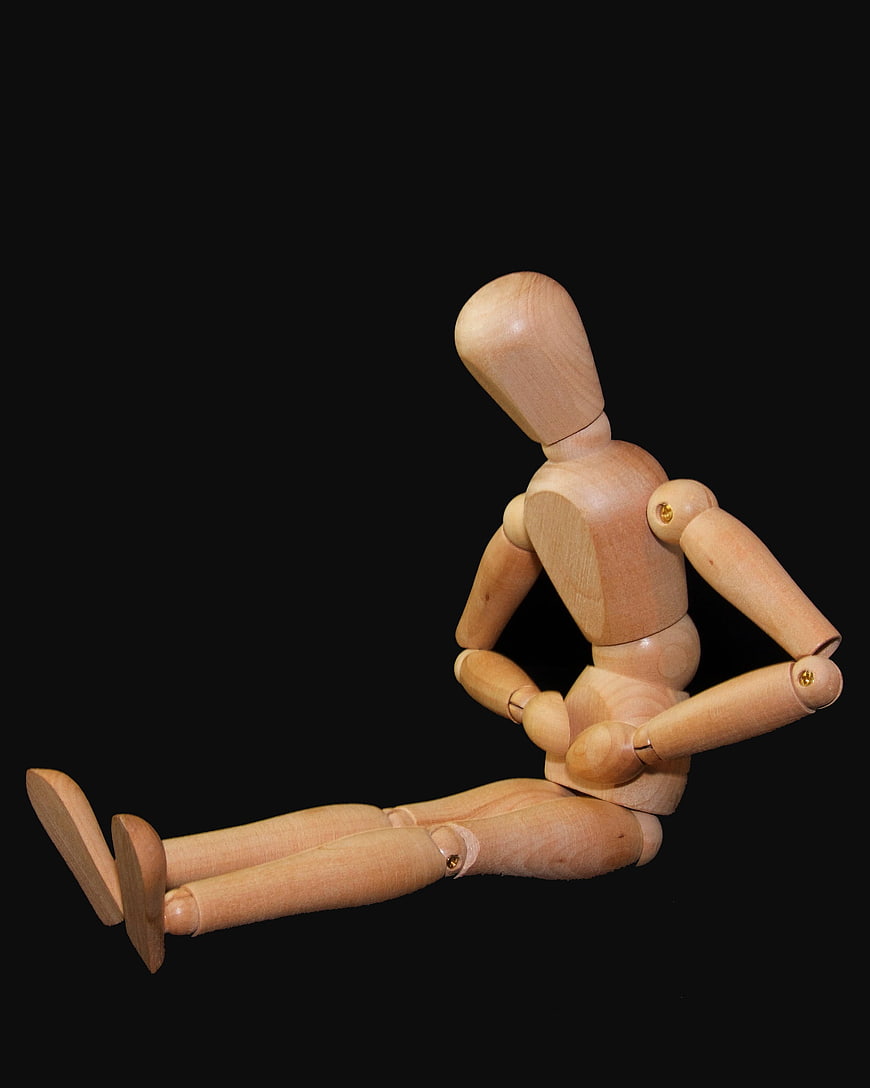 Wooden Mannequin Sitting with Stomach Ache on Black Background