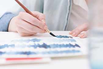 Close-up of hands painting with watercolor brush on paper