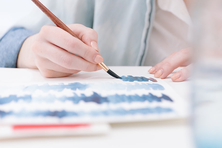 Close-up of hands painting with watercolor brush on paper
