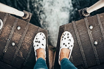 First-person view of feet in spotted shoes on wooden bridge edge