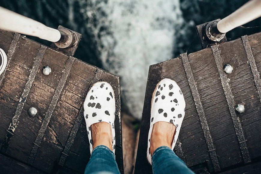 First-person view of feet in spotted shoes on wooden bridge edge
