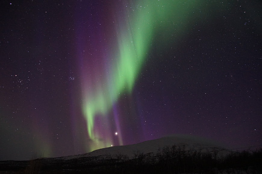 Green and purple aurora borealis over snowy winter landscape at night