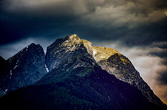 Dramatic Mountain Peak Illuminated by Sunlight Against Stormy Sky