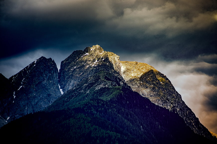 Dramatic Mountain Peak Illuminated by Sunlight Against Stormy Sky