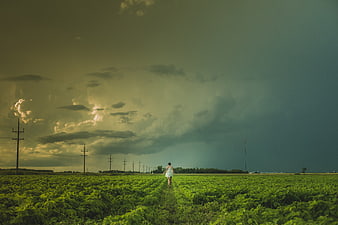 Woman in White Dress Walking Through Green Field Under Stormy Sky