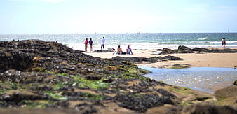 People relaxing on a rocky beach with ocean waves and sailboats