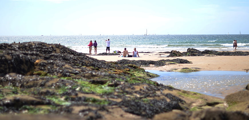 People relaxing on a rocky beach with ocean waves and sailboats