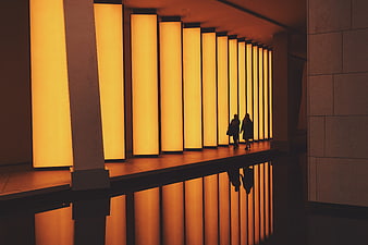Silhouettes of two people walking past glowing architectural columns