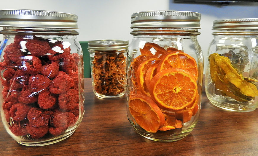 Mason jars filled with dried raspberries and orange slices on wood