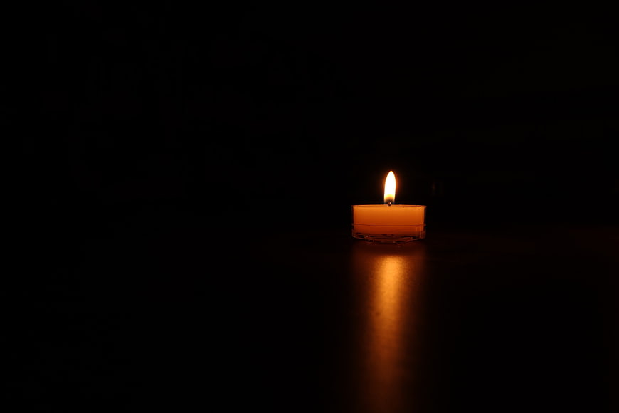 Single lit candle glowing in the dark with reflection