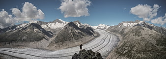 Panoramic view of hiker standing on rocky peak overlooking glacier